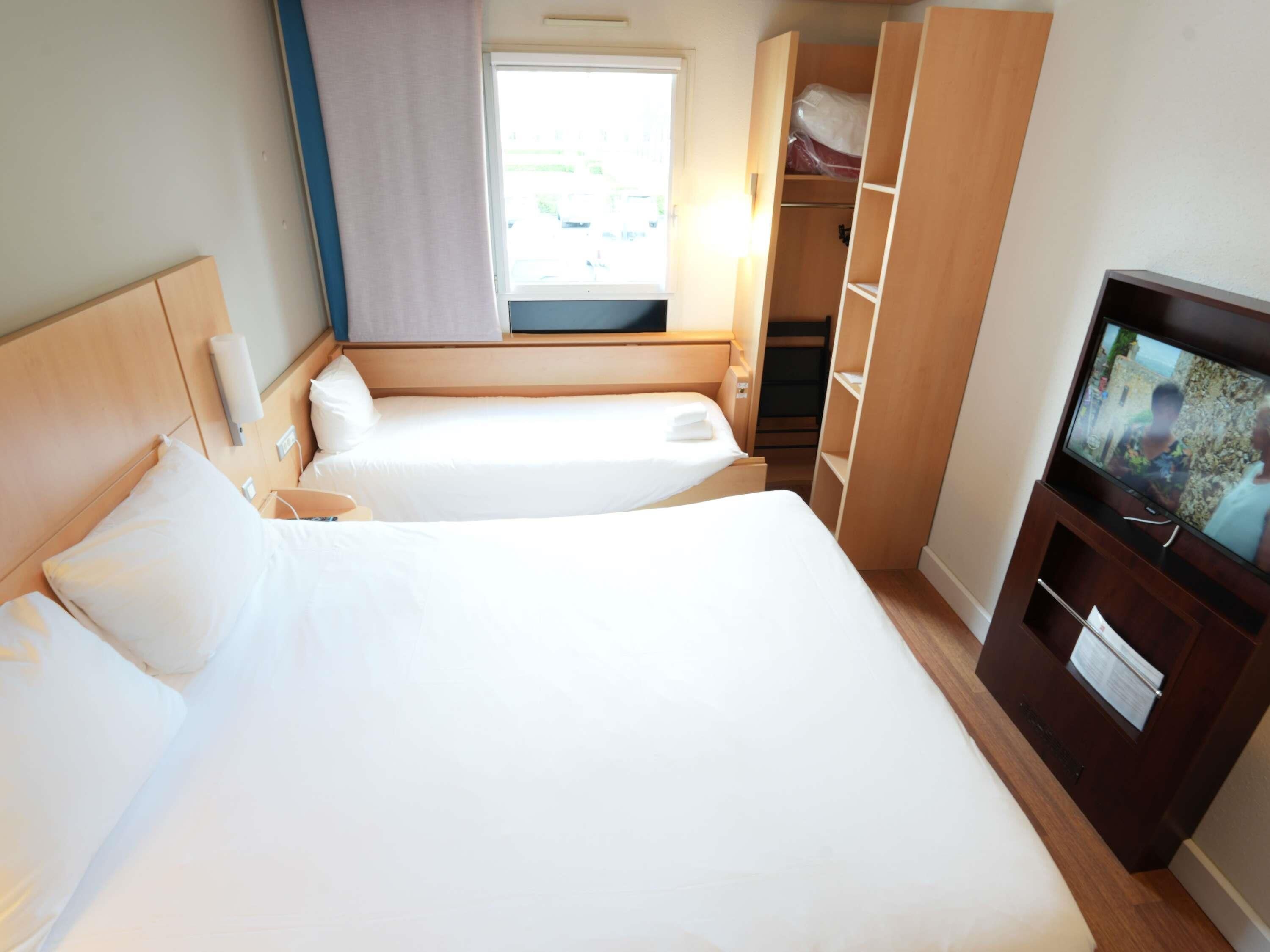 A hotel room with a large bed, a TV, a wardrobe, and a window with curtains.