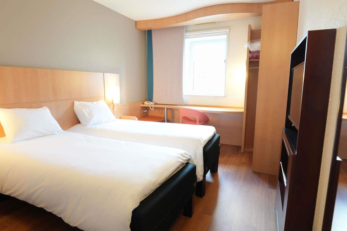 A hotel room with two beds, a desk, a chair, a TV, and a wardrobe.