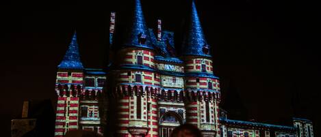 A castle-like structure with multiple spires and a clock tower, illuminated at night.