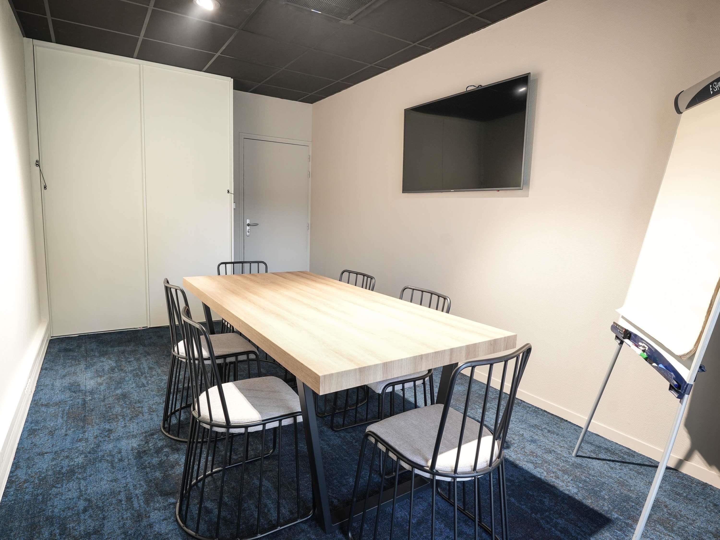 Una sala de conferencias con una mesa larga, seis sillas, una pizarra y un televisor de pantalla plana en la pared.