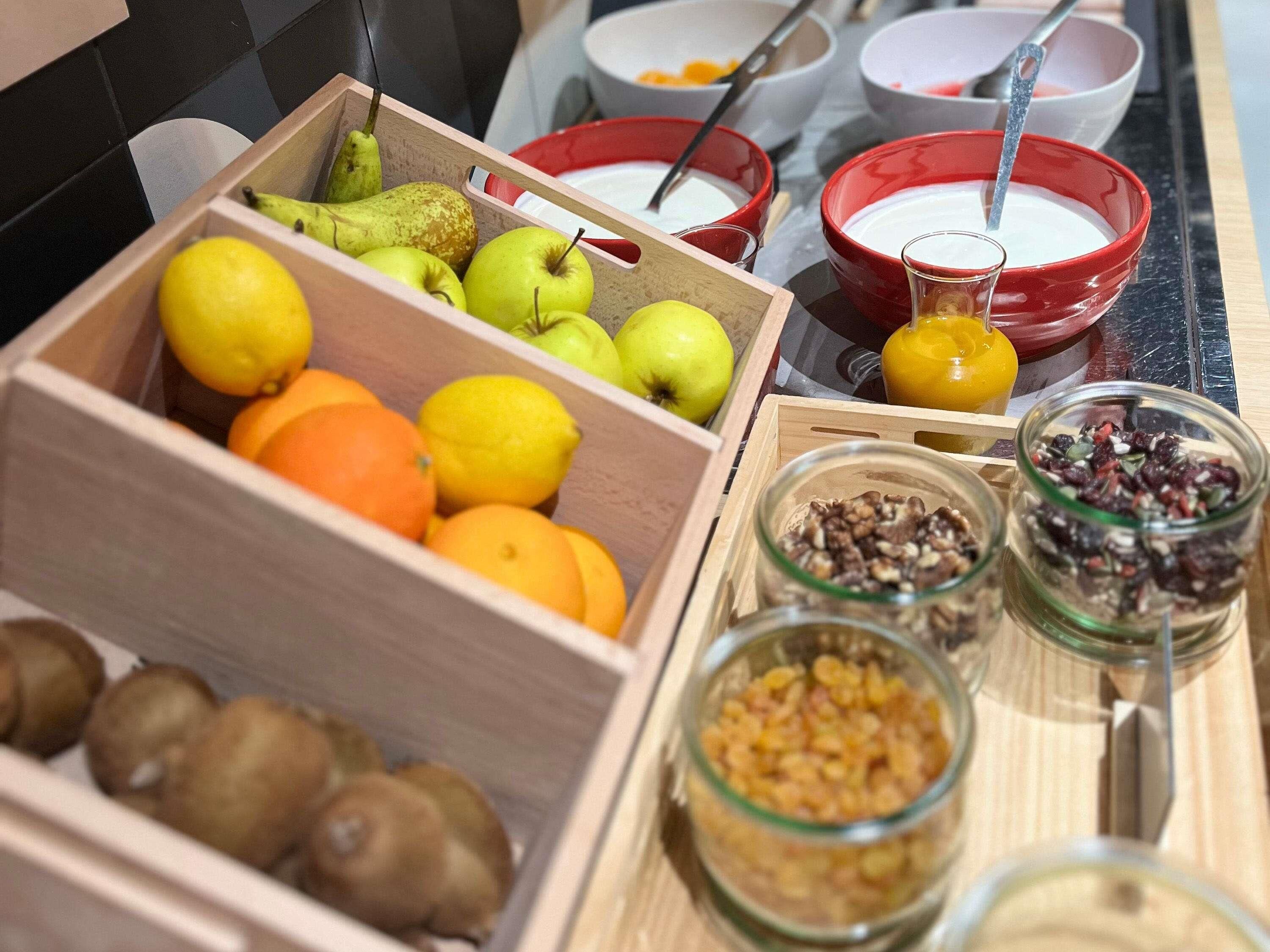 Eine Holzkiste mit Früchten, eine Schüssel Joghurt sowie Gläser mit Nüssen und Samen.