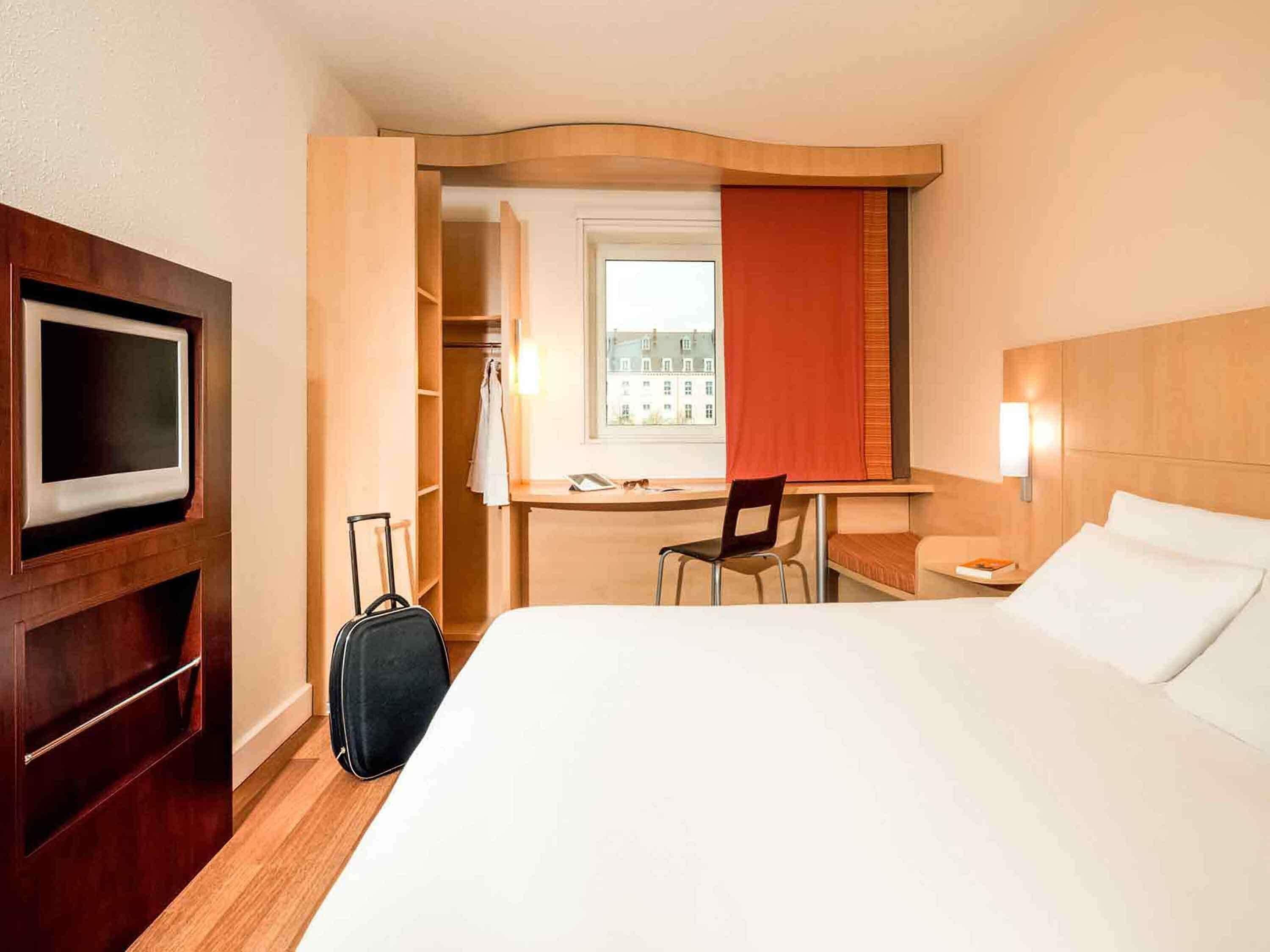 Ein Hotelzimmer mit Bett, Schreibtisch, Stuhl, Fernseher und Koffer.