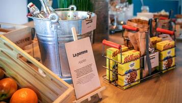 Una encimera de cocina con un cubo metálico que dice 'La pomme', una caja de madera con manzanas y una exhibición de cajas de cereal Kellogg's.