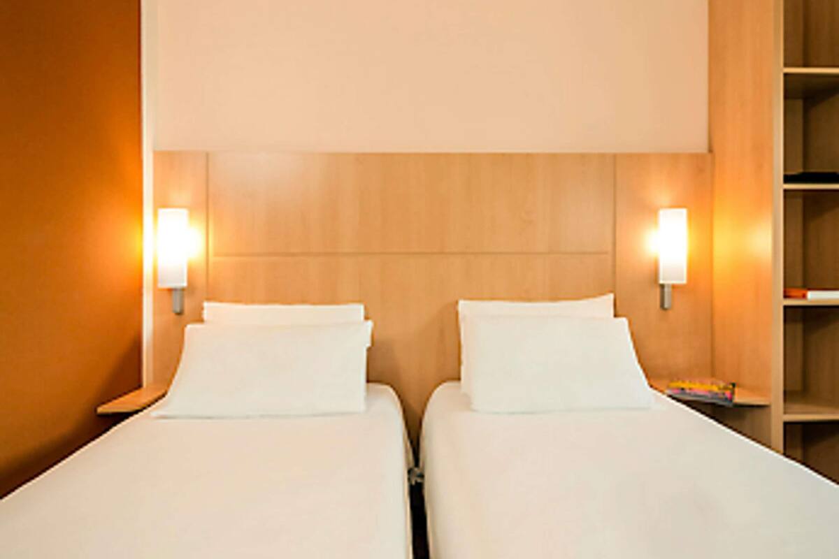 Quarto de hotel com duas camas, peseira de madeira e luminárias fixadas na parede.
