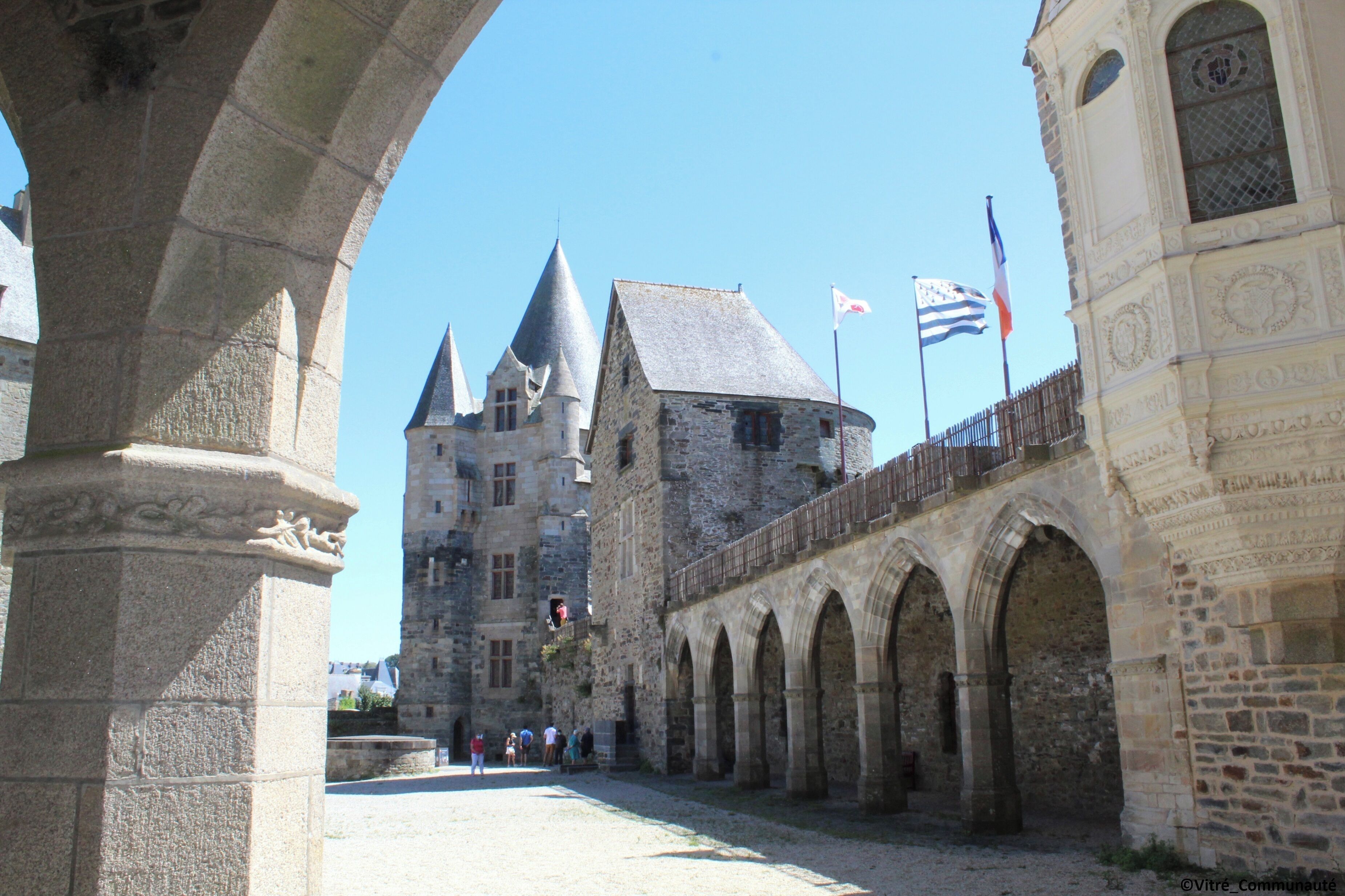A historic stone building with a central tower, arched walkways, and flags.