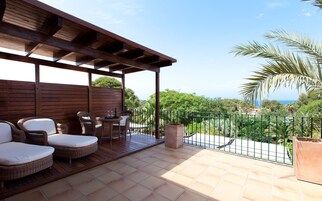 A covered outdoor seating area with wicker furniture and a view of the sea.