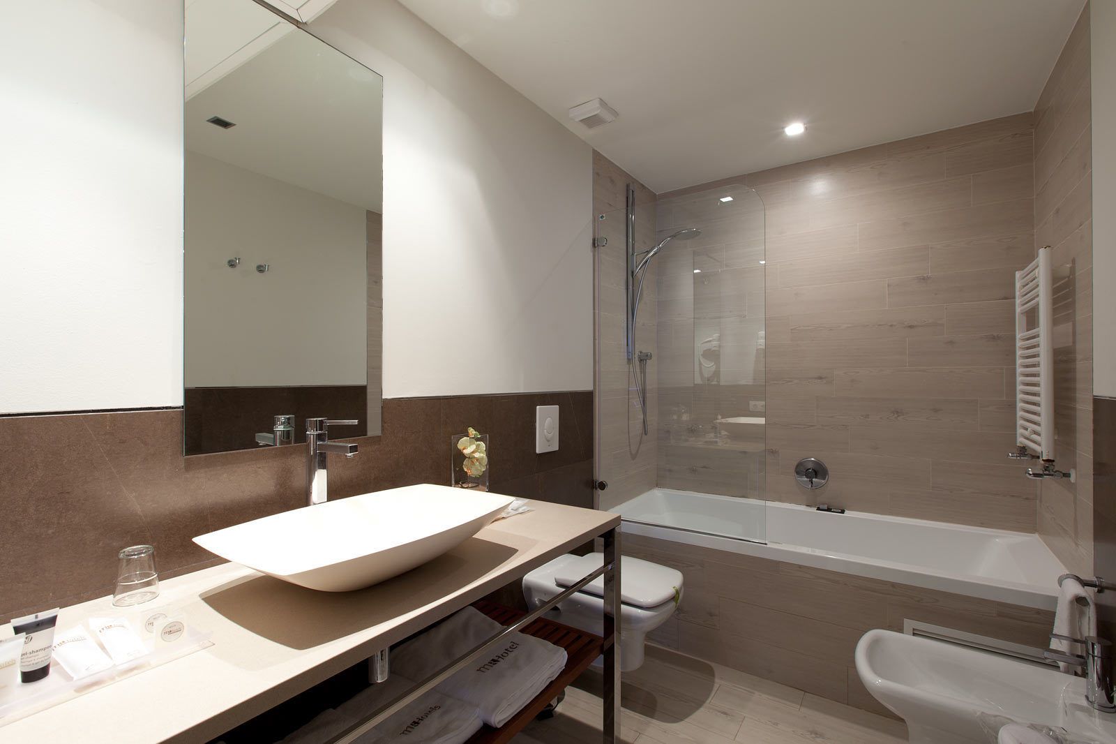 Un baño moderno con un lavamanos grande de color blanco, ducha con mampara de vidrio y un inodoro.