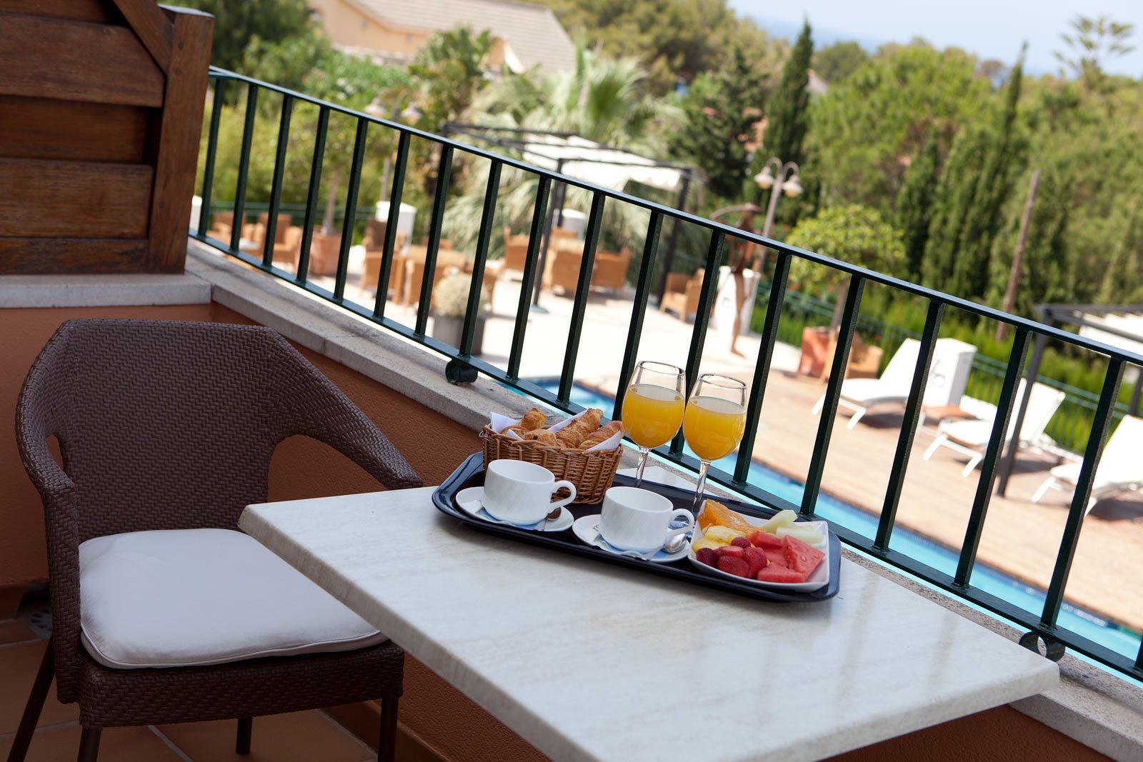 A balcony with wicker furniture, a tray with breakfast items, and a pool view.