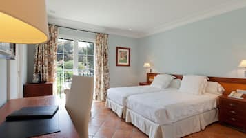 A hotel room with two beds, a desk, a chair, and a view of the outdoors.