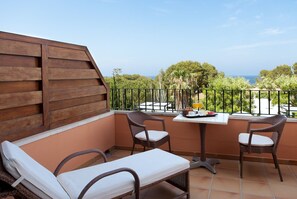 A balcony with wicker furniture, a table with breakfast items, and a scenic view of trees and the sea. - Hotel Les Rotes (Denia)