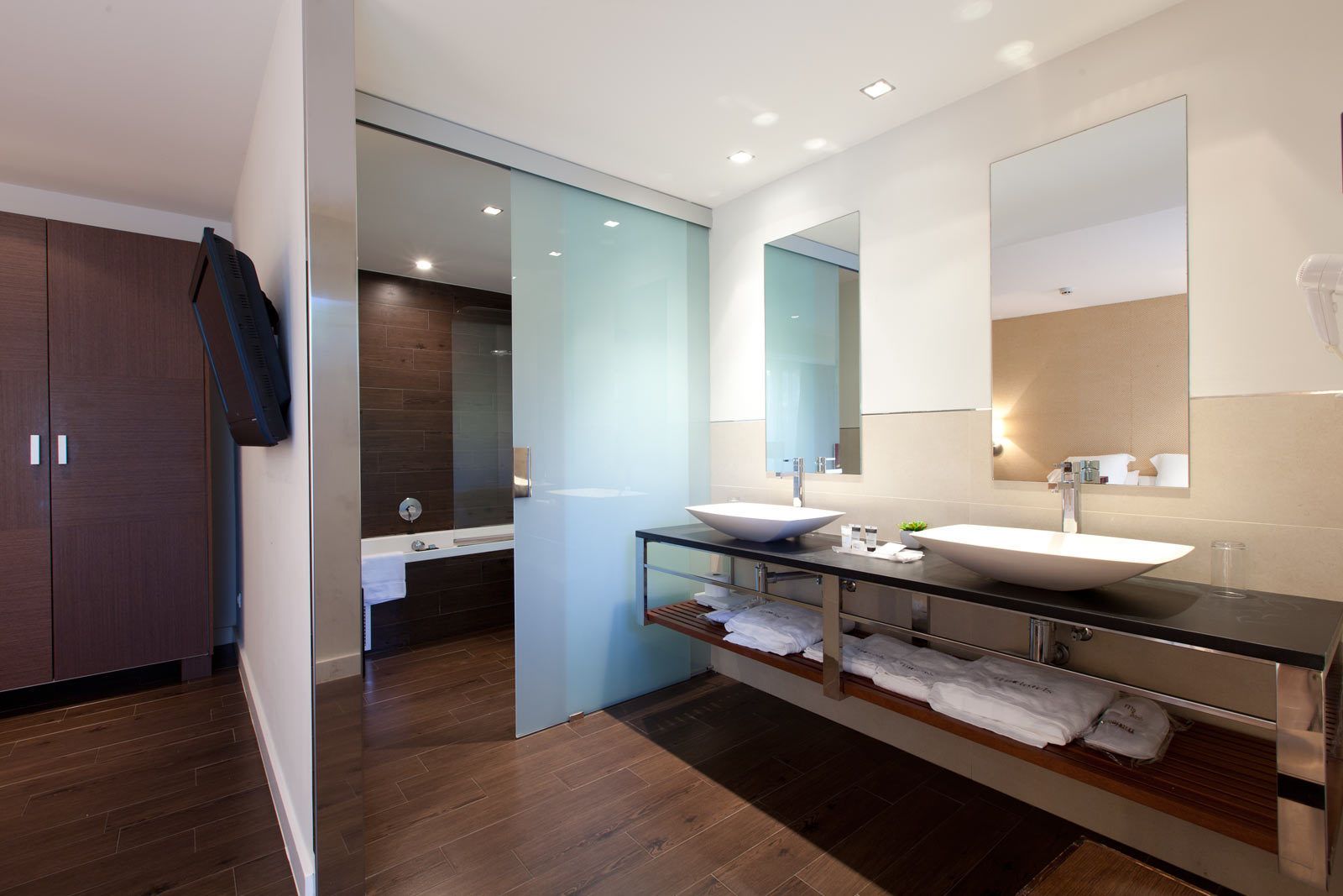 A modern bathroom with a large mirror, two sinks, and a shower area.