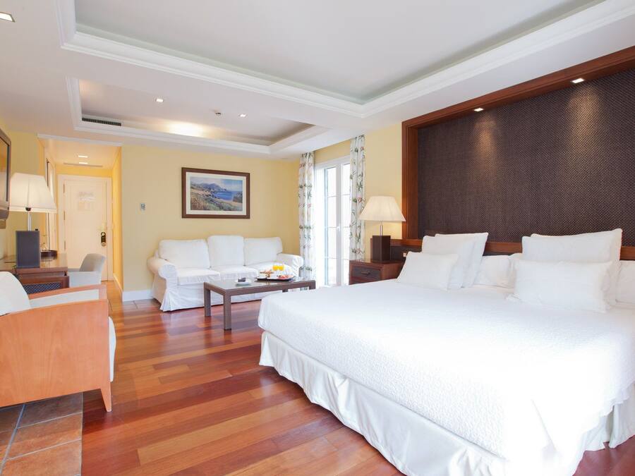 Una habitación de hotel con una cama grande, un sofá, una mesita con artículos para el desayuno y un televisor.