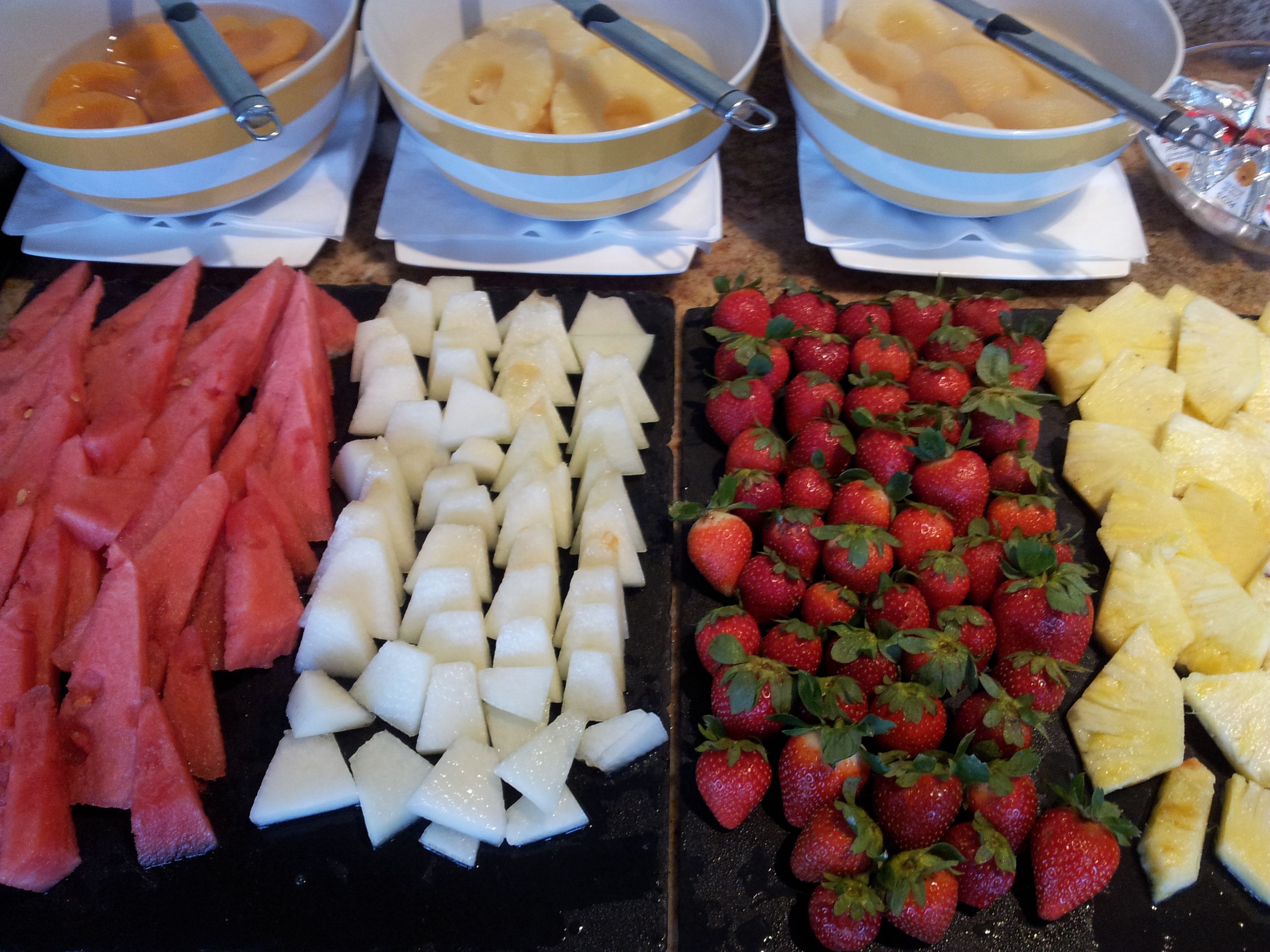 A kitchen counter with bowls of fruit, including watermelon, pineapple, and strawberries.