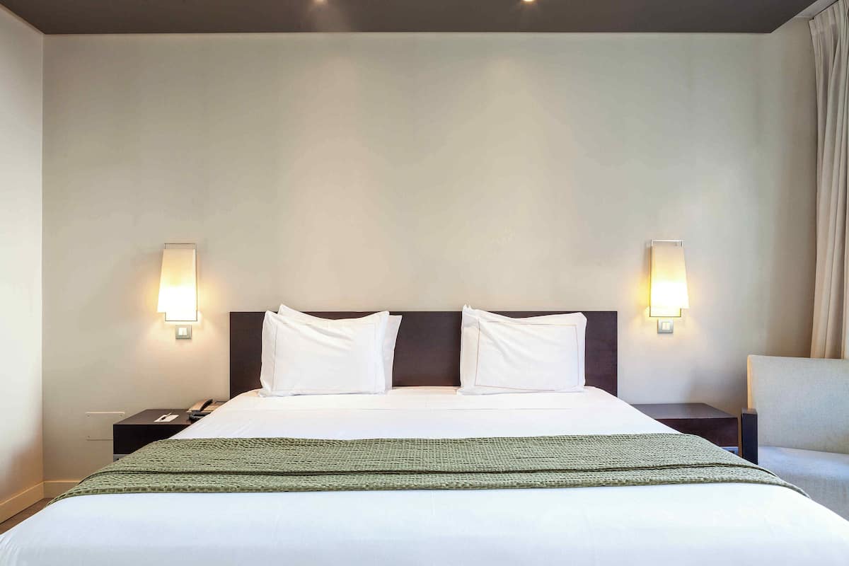 A hotel room with a large bed, two bedside tables, a chair, and wall-mounted lights.