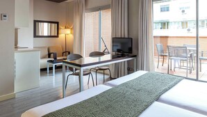 A hotel room with a bed, a desk with a TV, a chair, a sofa, and a balcony with chairs. - Suites Viena Plaza de España (Madrid)