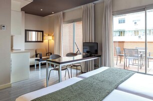 A hotel room with a bed, a desk with a TV, a chair, a sofa, and a balcony with chairs.