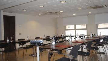 Een congreszaal met lange tafels, stoelen en een beamer.