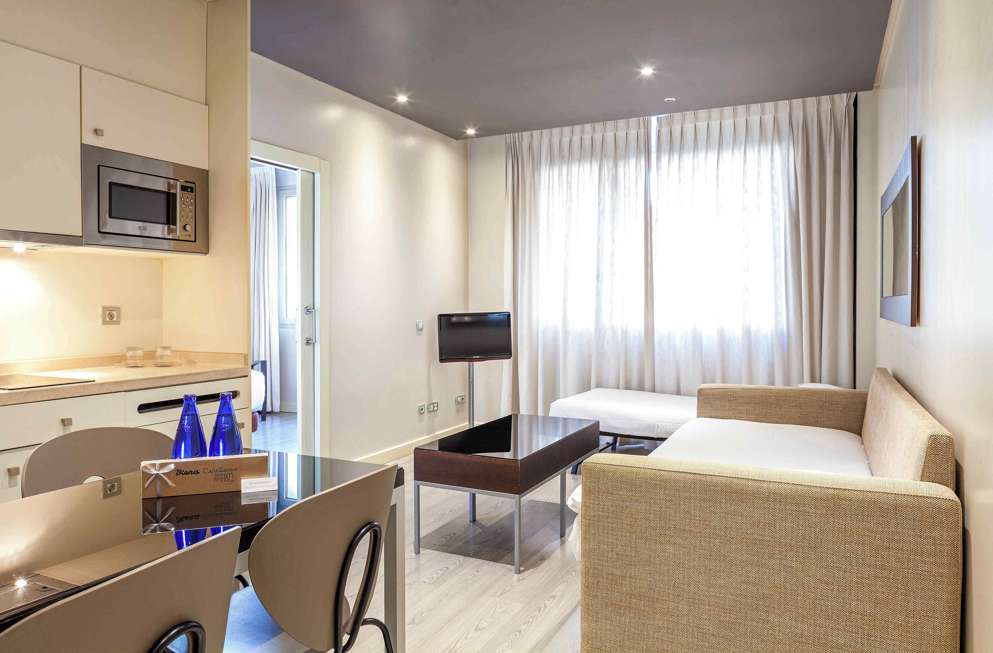 Habitación de hotel con kitchenette, televisor de pantalla plana, sofá y zona de comedor con sillas.