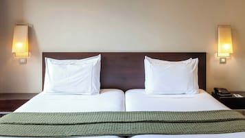 A double bed with white linens, two pillows, a green throw blanket, and two wall-mounted lamps on either side.