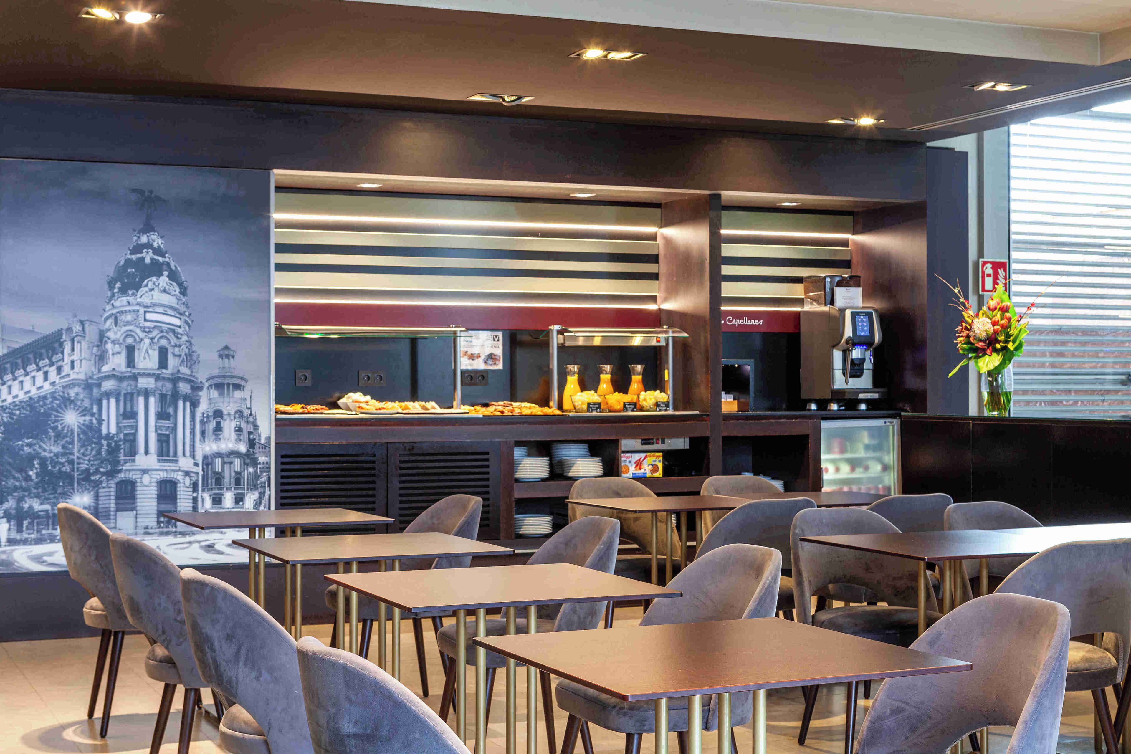 A restaurant with tables and chairs, a counter with a coffee machine, and a mural on the wall.