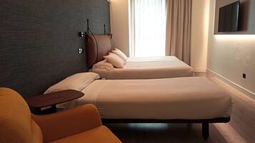 A hotel room with two beds, a wooden headboard, a TV mounted on the wall, and a window with curtains.