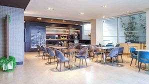 A modern restaurant with a bar area, seating with tables and chairs, and large windows with plants. - Suites Viena Plaza de España (Madrid)