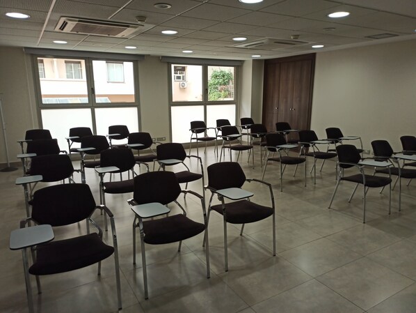 Un salón de conferencias con filas de sillas y mesas, ventanas amplias e iluminación empotrada en el techo.