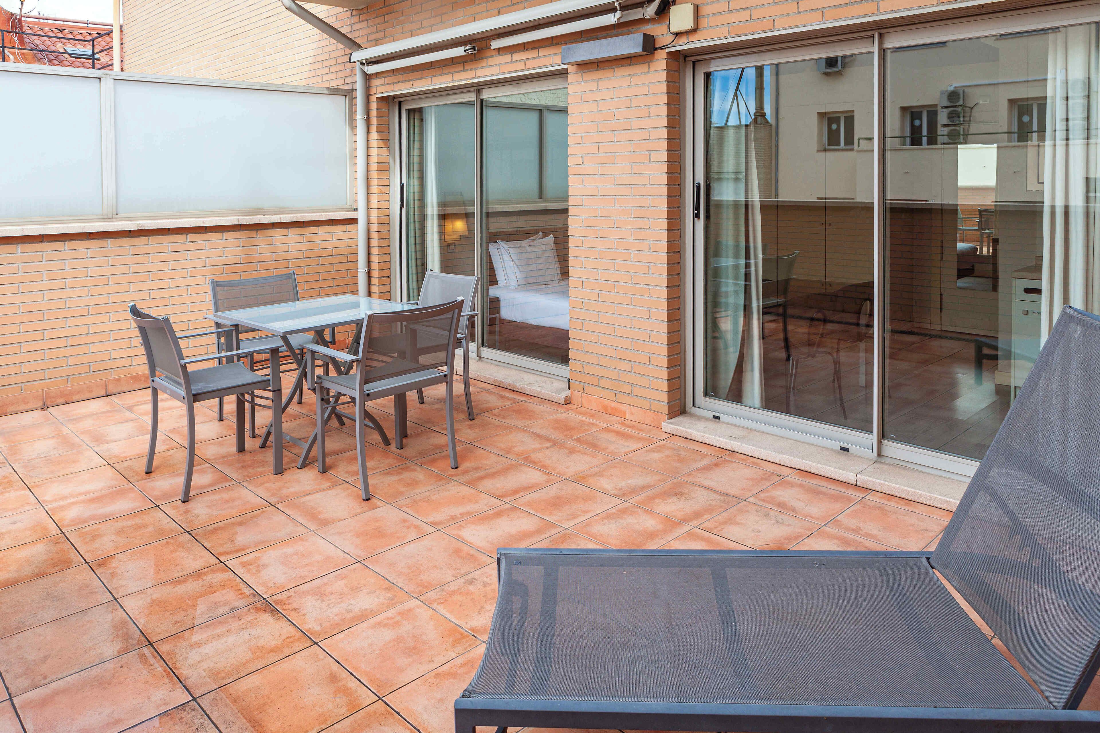 Patio con tavolo e sedie, un letto con una porta finestra e vista sulla strada.