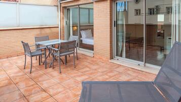 Patio con tavolo e sedie, un letto con una porta finestra e vista sulla strada.
