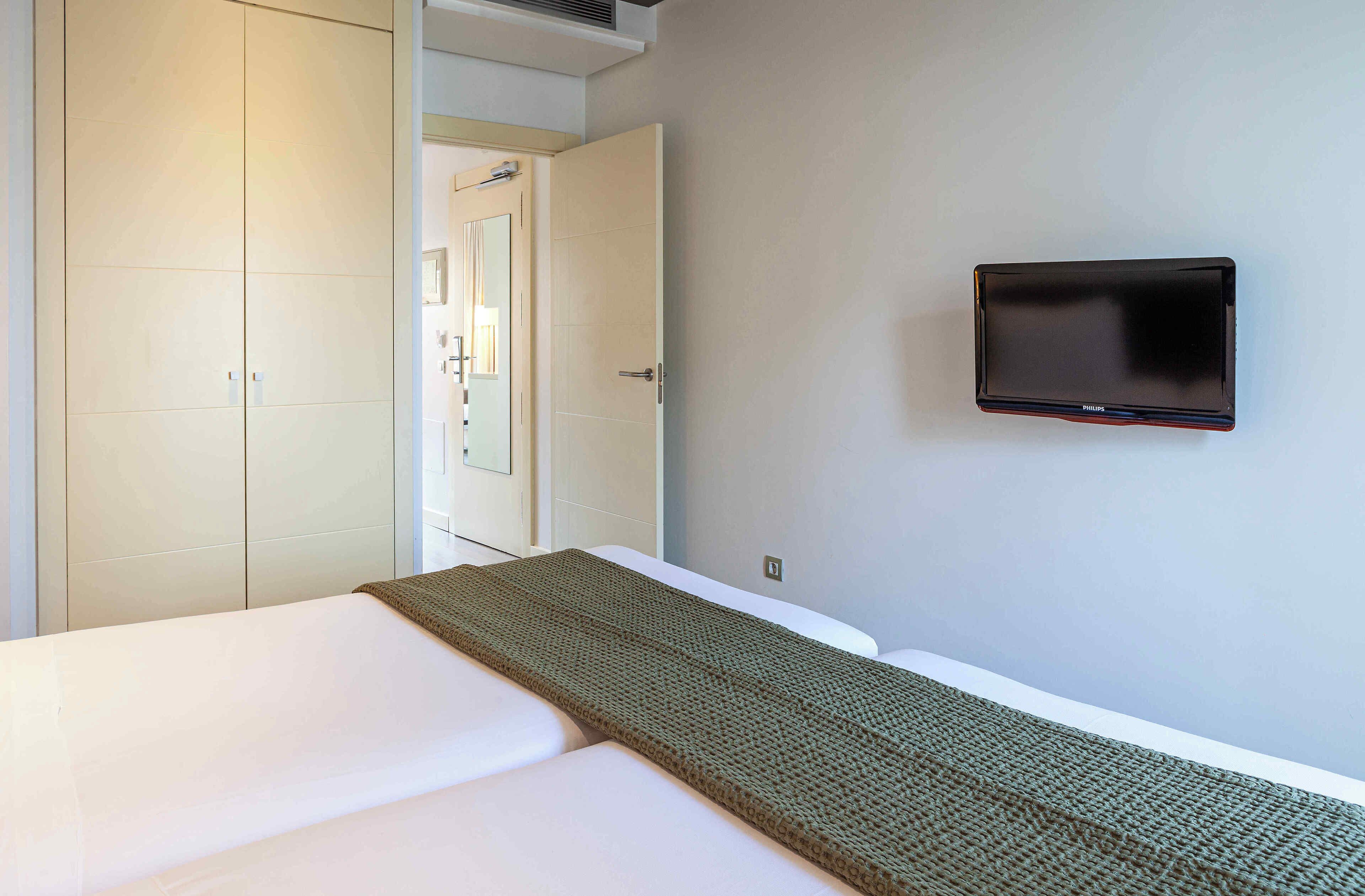 A hotel room with a bed, a television mounted on the wall, and a door leading to another room.