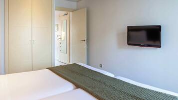 Una habitación de hotel con una cama, un televisor montado en la pared y una puerta que da a otra habitación.