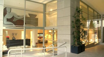 A modern hotel lobby with glass walls, a reception desk, and a large potted plant.