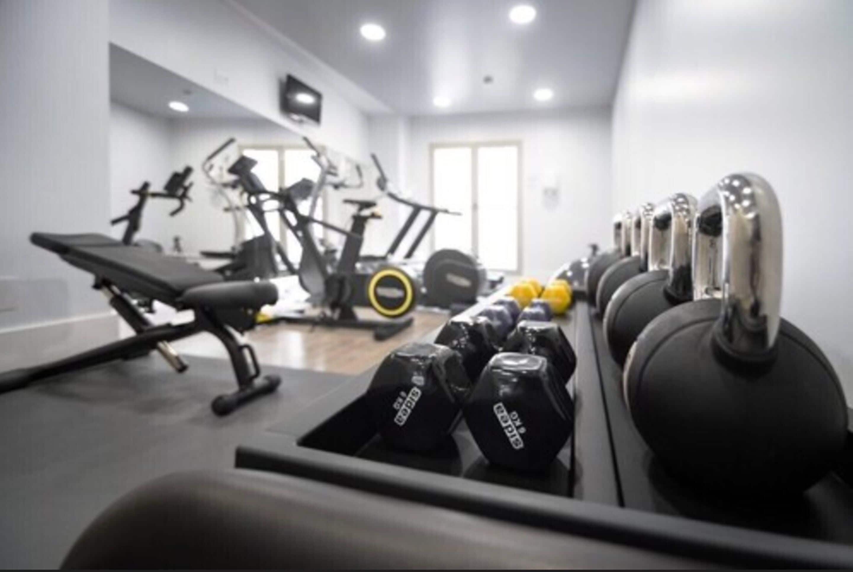 Un gimnasio con equipo de ejercicio, incluyendo pesas, banco y máquinas de cardio.