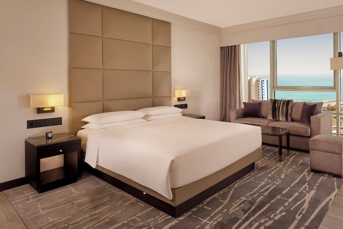 Quarto de hotel com uma cama grande, um sofá, uma mesa pequena e vista para o oceano.