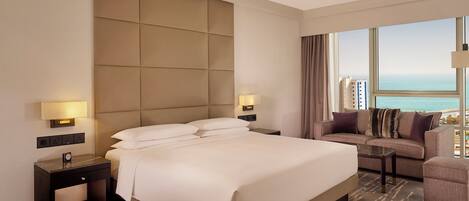 Habitación de hotel con una cama grande, un sofá, una mesita y vista al océano.