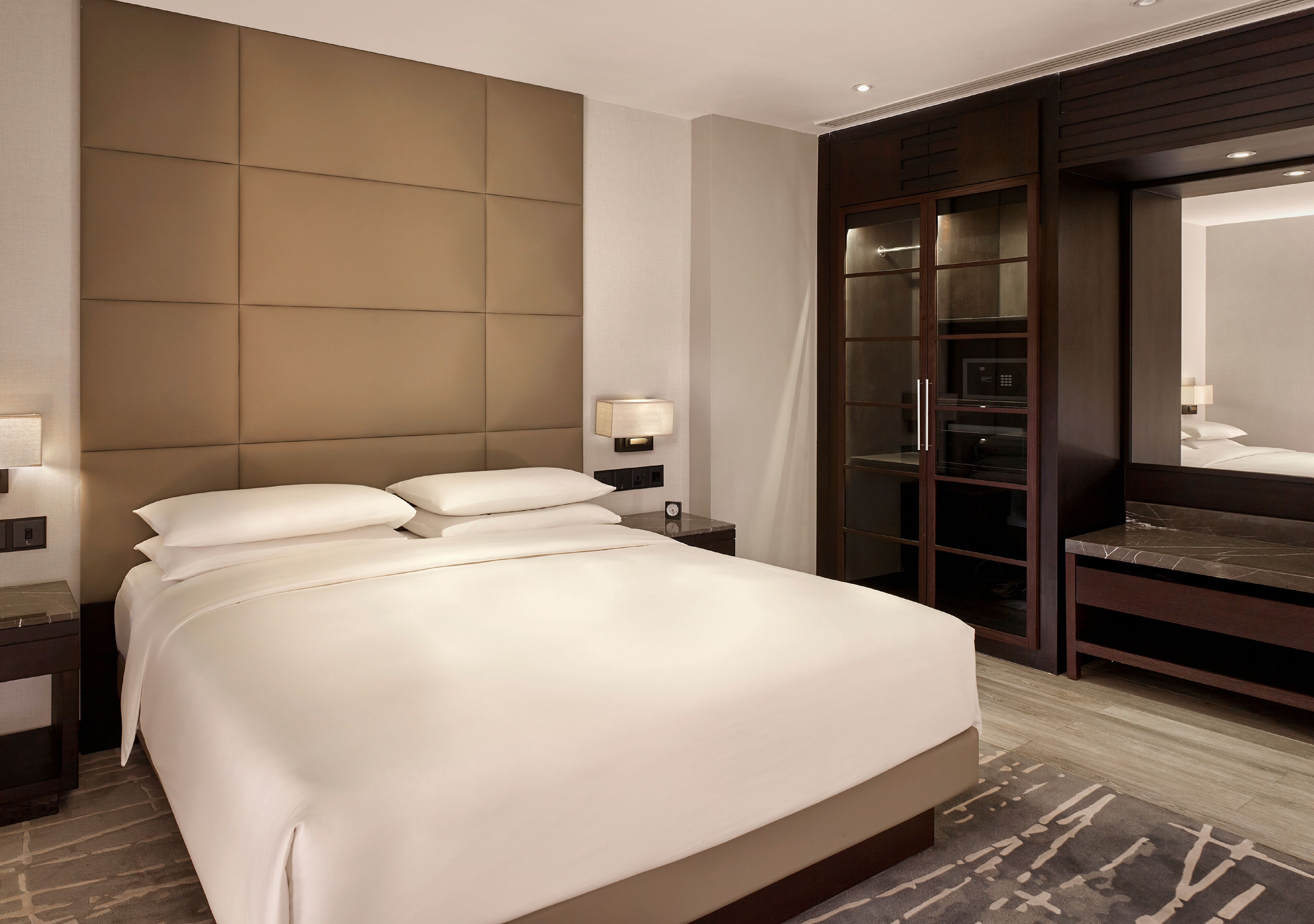 A hotel room with a large bed, a wardrobe, a mirror, and a nightstand with a lamp.