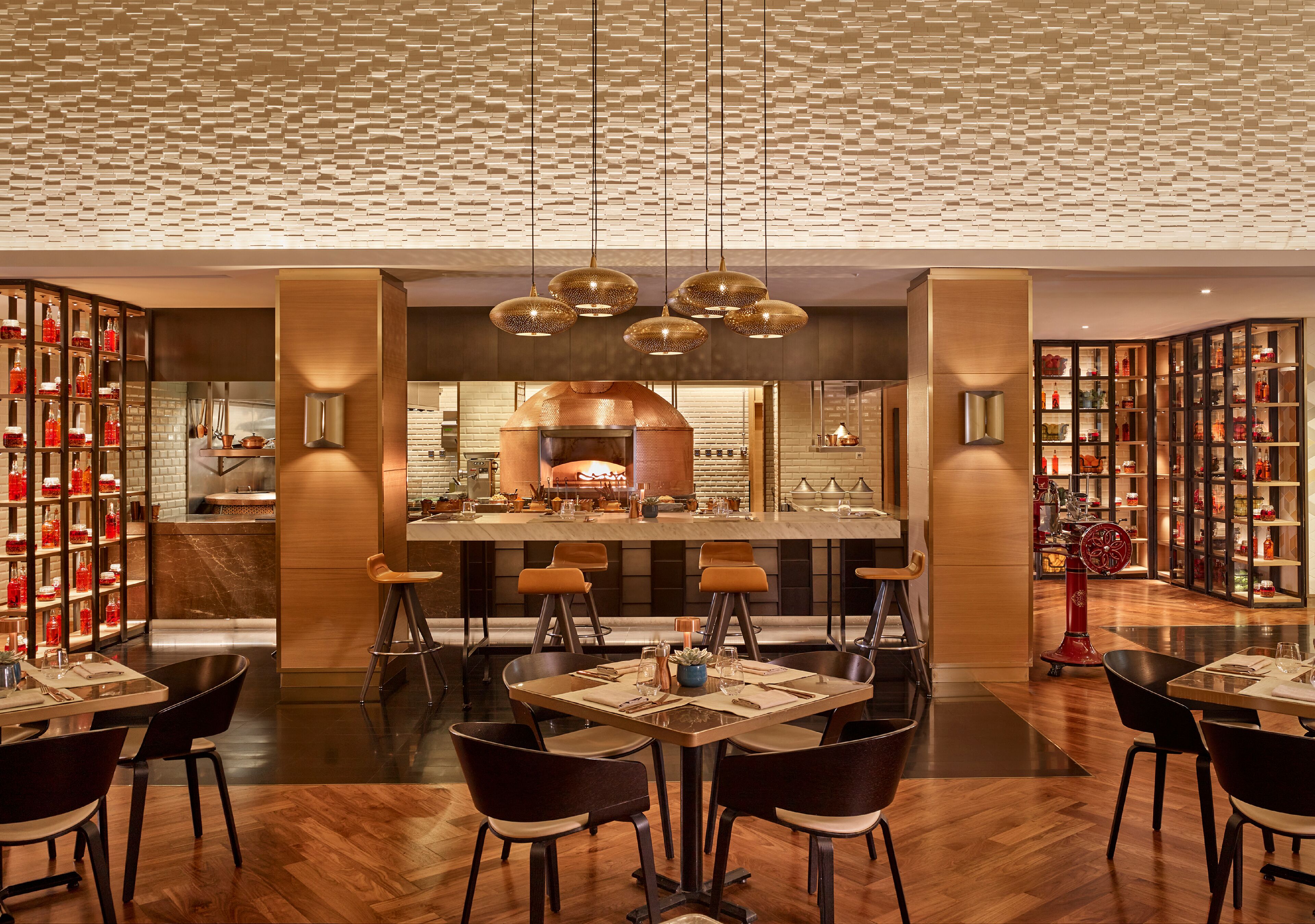 A modern restaurant with a central bar, multiple seating areas, and a patterned ceiling.