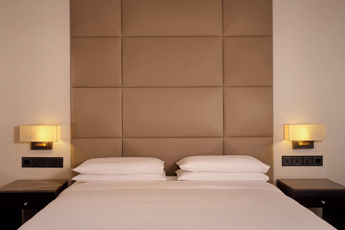 Una habitación de hotel con una cama grande, dos lámparas de noche y un cabecero con diseño acolchado.