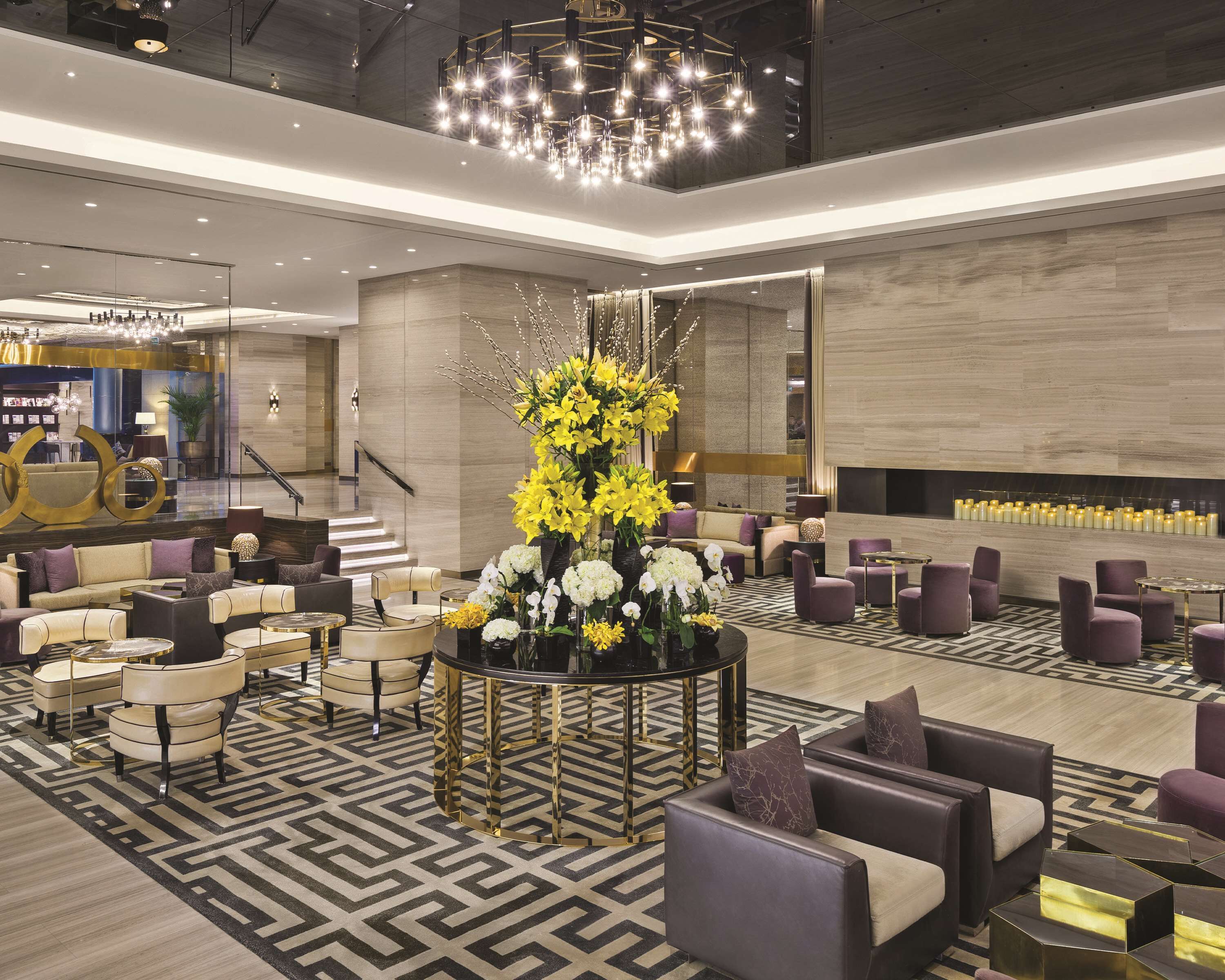 A modern lobby with a central floral arrangement, seating areas, and a staircase.