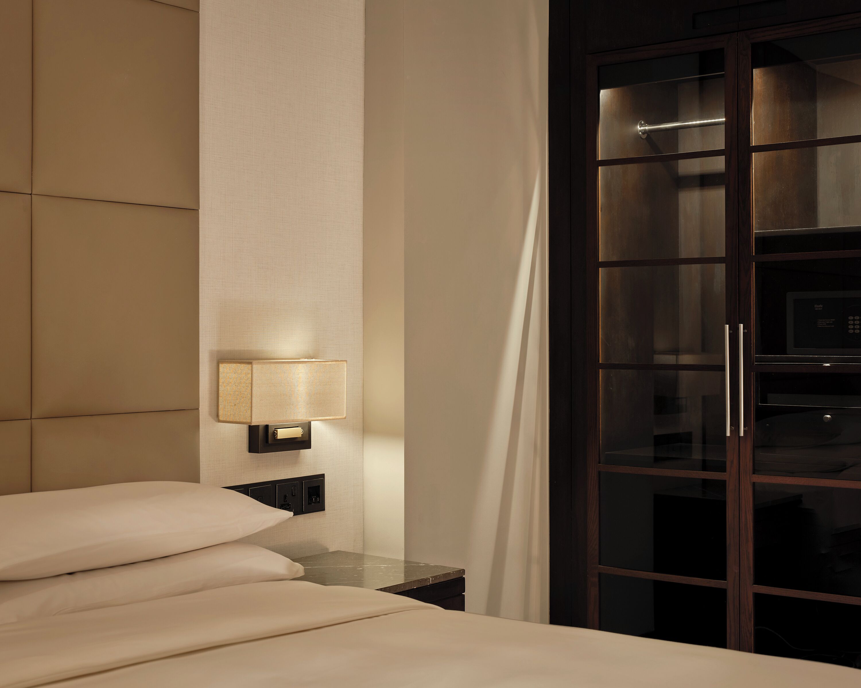 Habitación de hotel con cama, mesita de noche con lámpara, ventana con cortinas y un microondas visible a través de la ventana.
