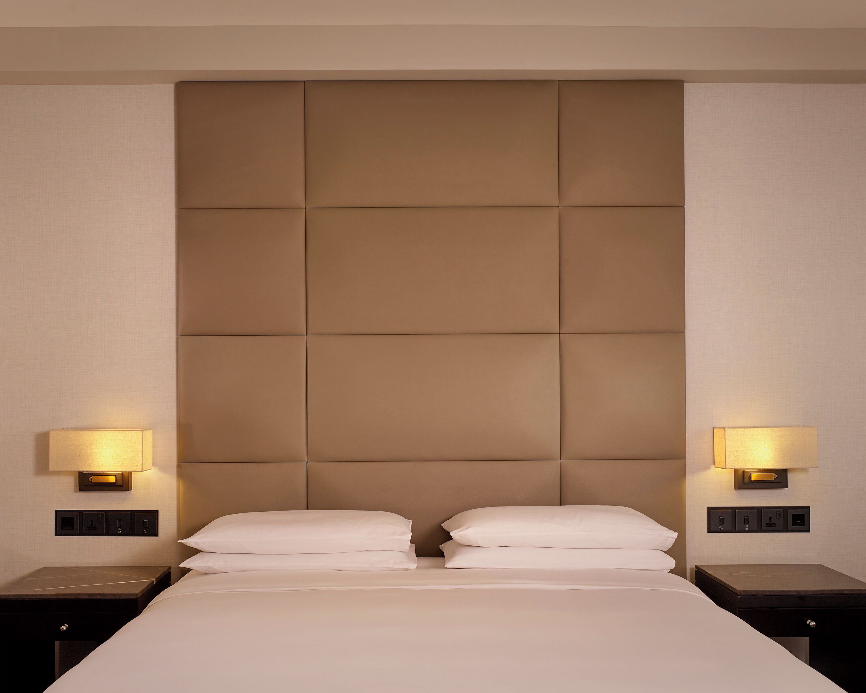 Ein Hotelzimmer mit einem großen Bett, zwei Nachttischlampen und einem gepolsterten Kopfteil.