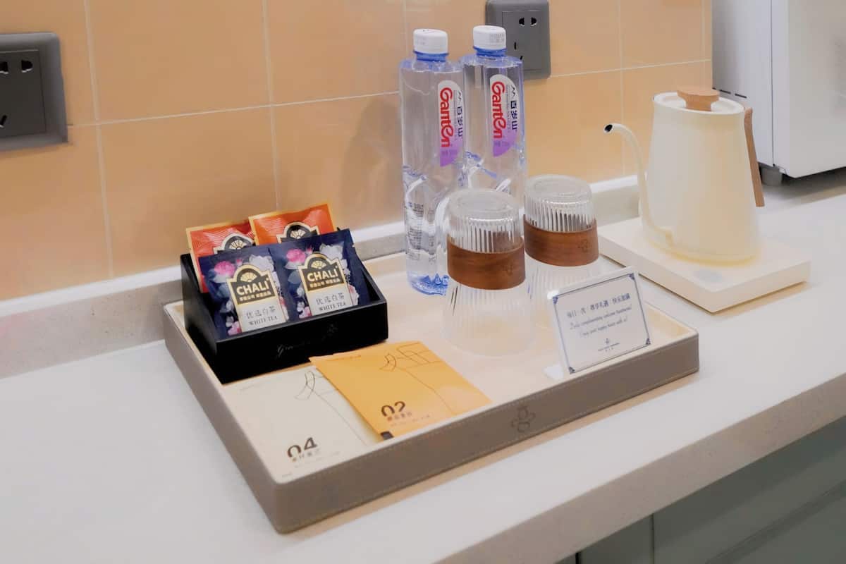 A hotel room counter with a tray containing tea bags, bottled water, and a coffee pot.