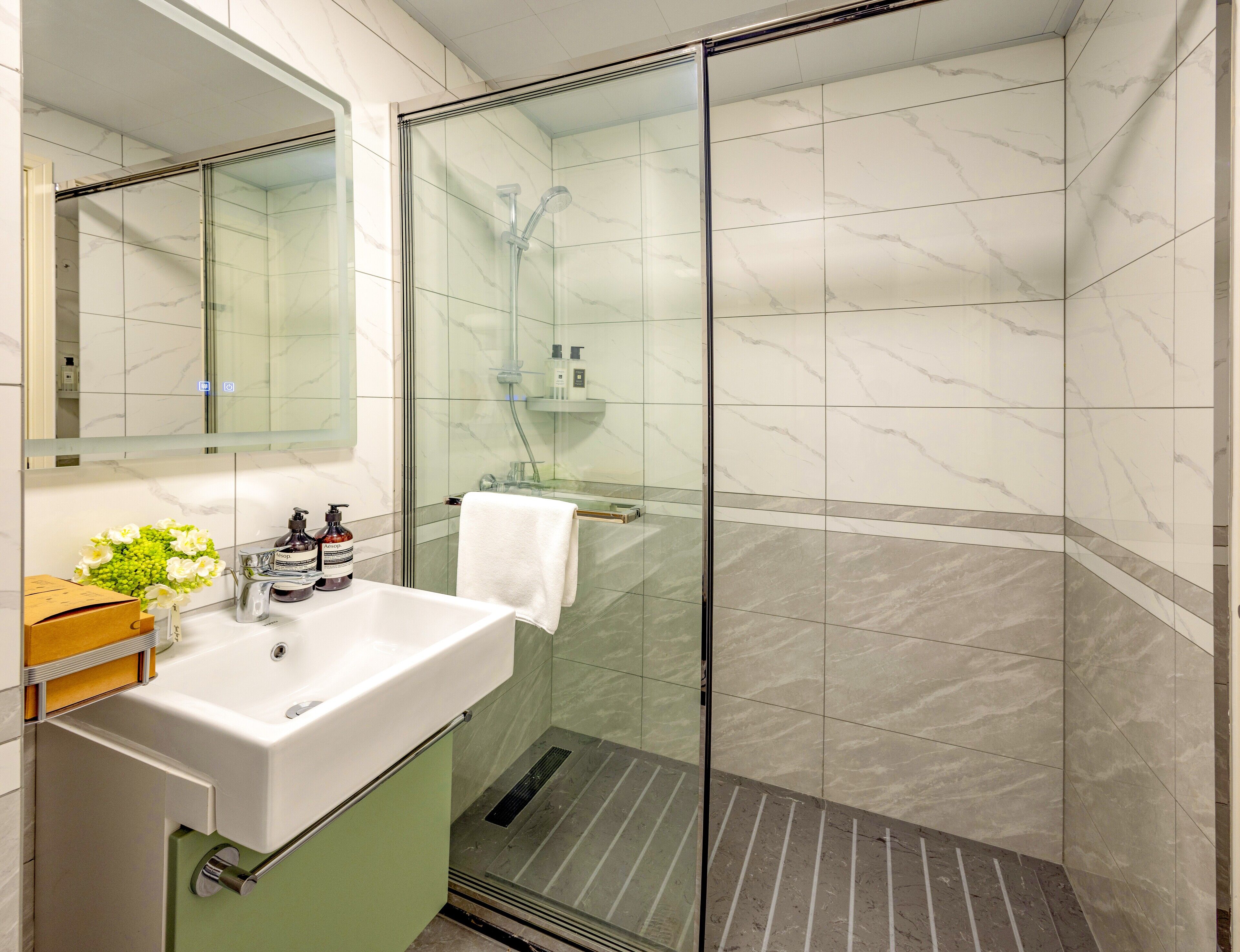 A modern bathroom with a glass-enclosed shower, a white sink with a green cabinet, and a mirror above the sink.