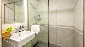 A modern bathroom with a glass-enclosed shower, a white sink with a green cabinet, and a mirror above the sink.