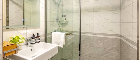 A modern bathroom with a glass-enclosed shower, a white sink with a green cabinet, and a mirror above the sink.