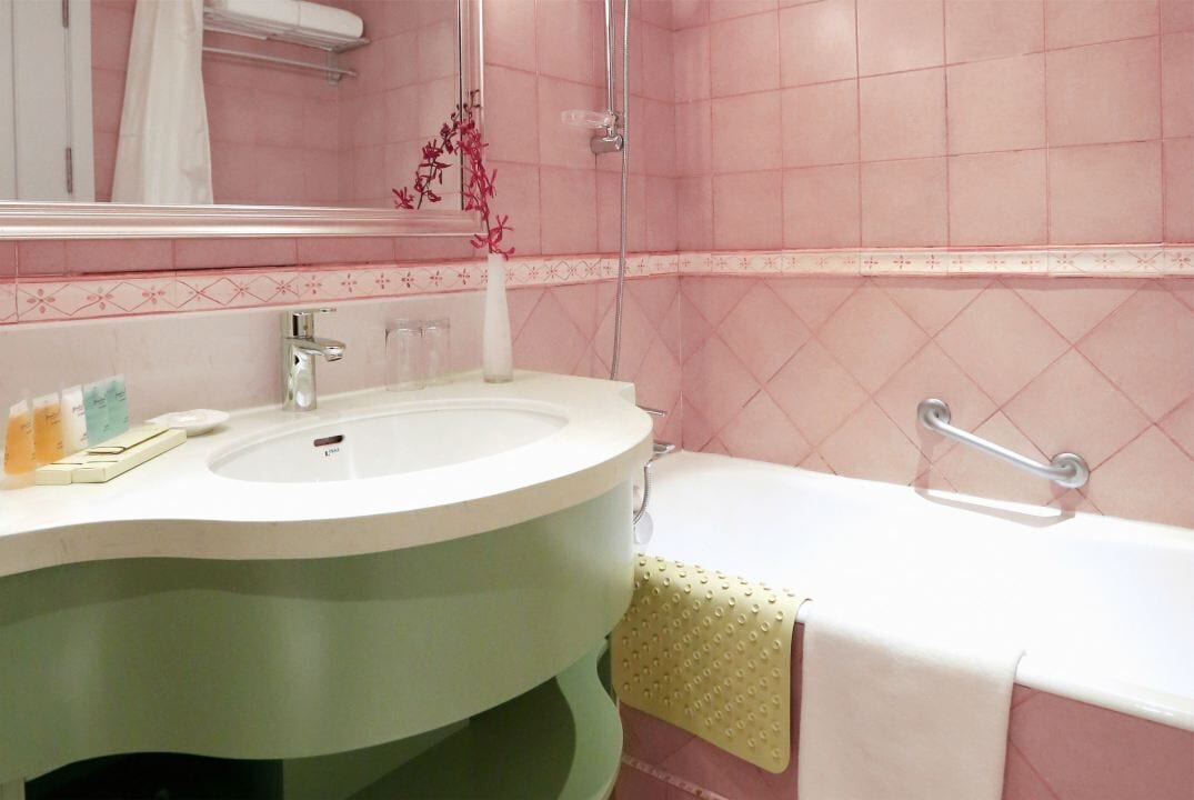 Een badkamer met een wastafel, spiegel, douche en een greepstaaf.