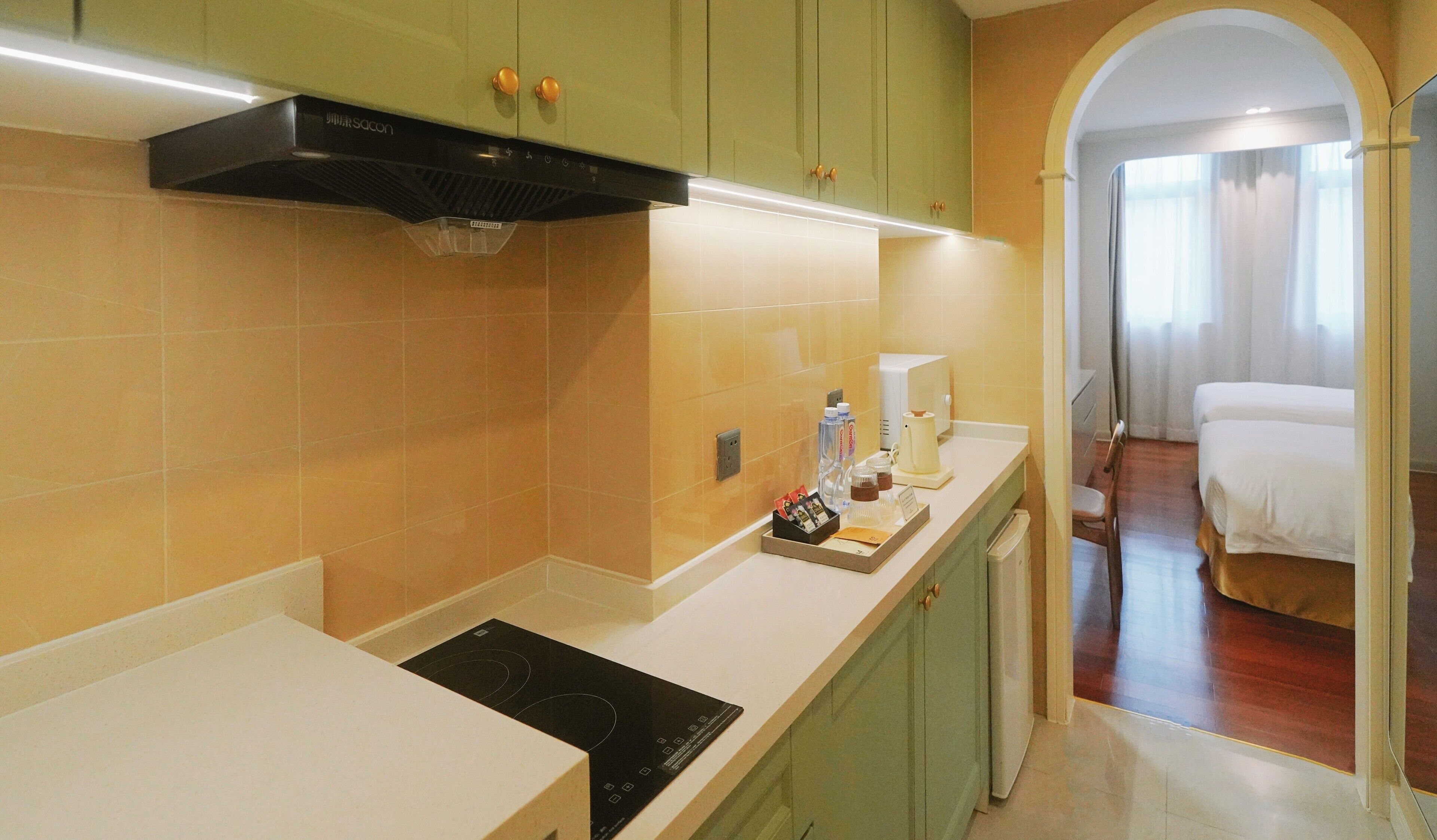 A modern kitchen with green cabinets, a black range hood, and a countertop with a coffee maker and water bottles.