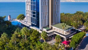 A modern building with a large glass facade, a rooftop pool, and a view of the sea. - Delta Hotels Antalya Lara (Antalya)