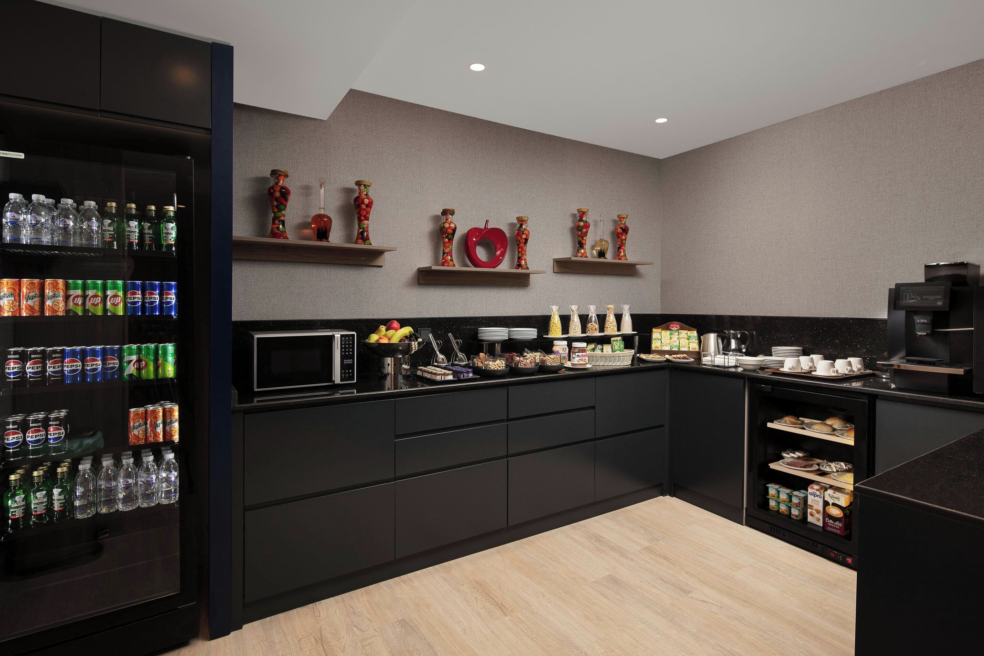 A modern kitchen with a refrigerator stocked with beverages, a microwave, and various food items on the counter.