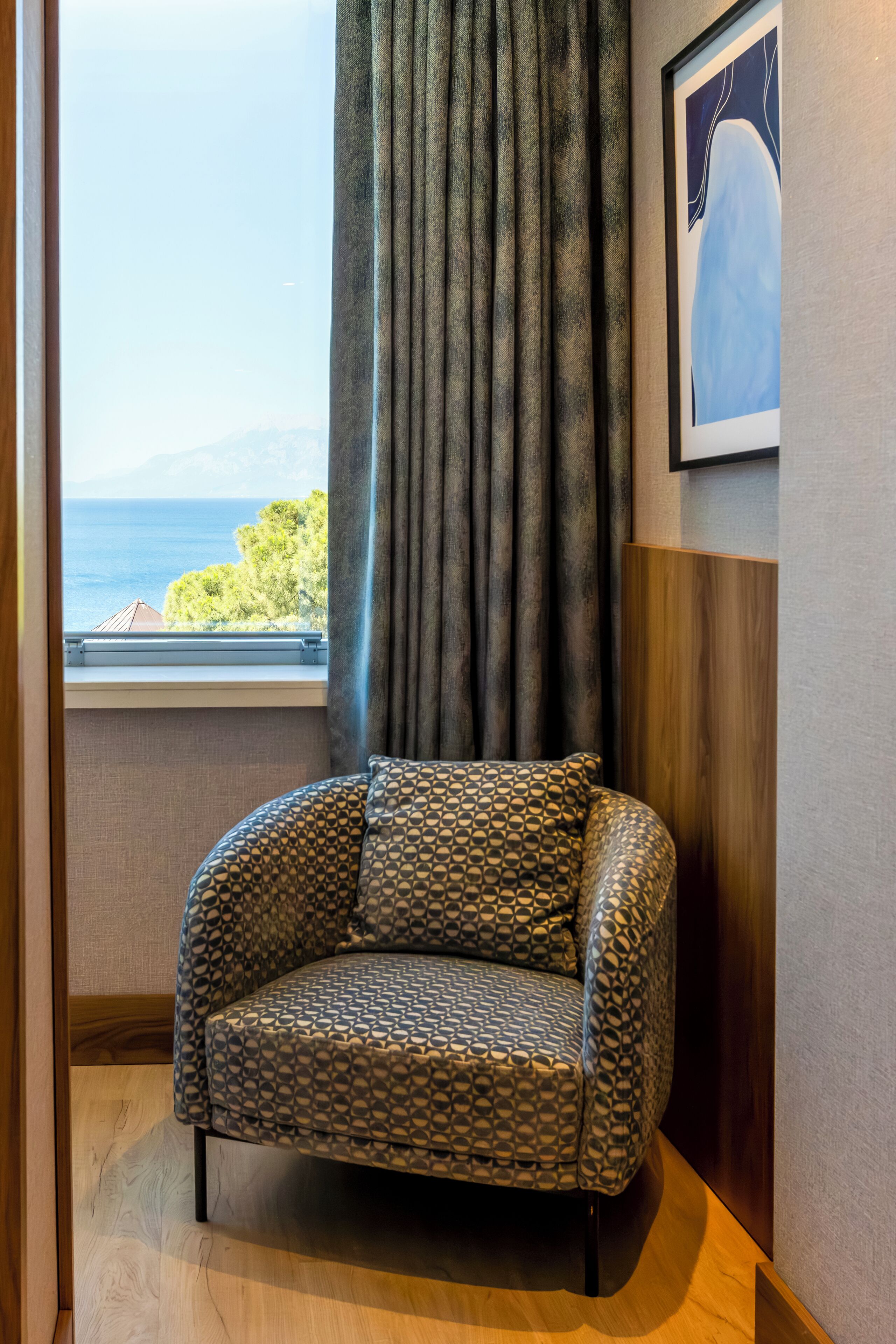 Une chambre d’angle avec vue sur la mer, un fauteuil à motifs et une œuvre d’art encadrée au mur.